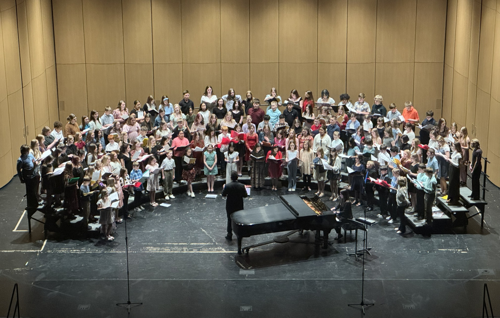 A photo of a stage with a lot of choir members standing on the risers, performing at the SWICDA Honor Choir.