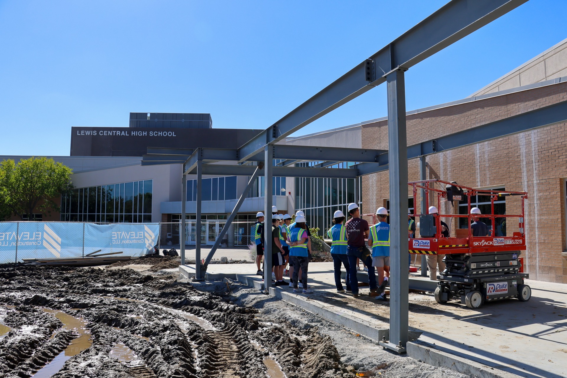 A photo of the entrance of Lewis Central High School during construction of the new entrance and safety vestibule with students in hard hats touring the project.