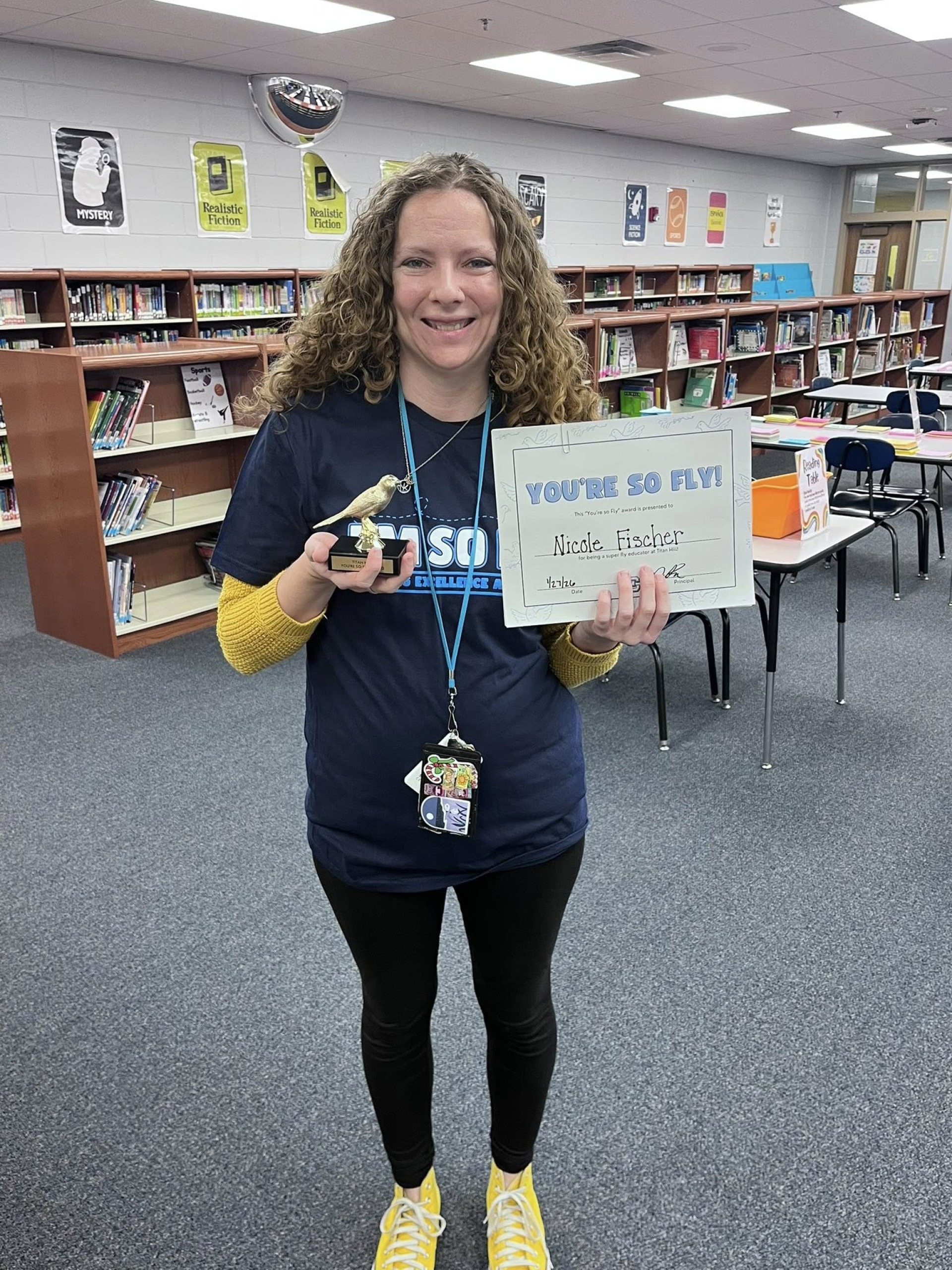 Miss Fischer, 2nd and 3rd grade art teacher, holding her "You\'re So Fly" staff award.
