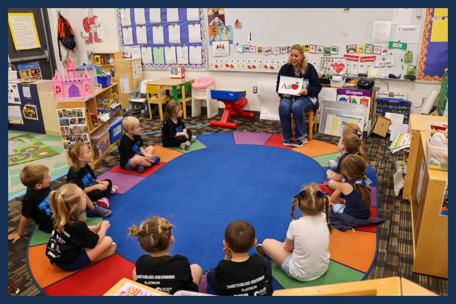 Preschool classroom with students sitting on the floor being read a book.
