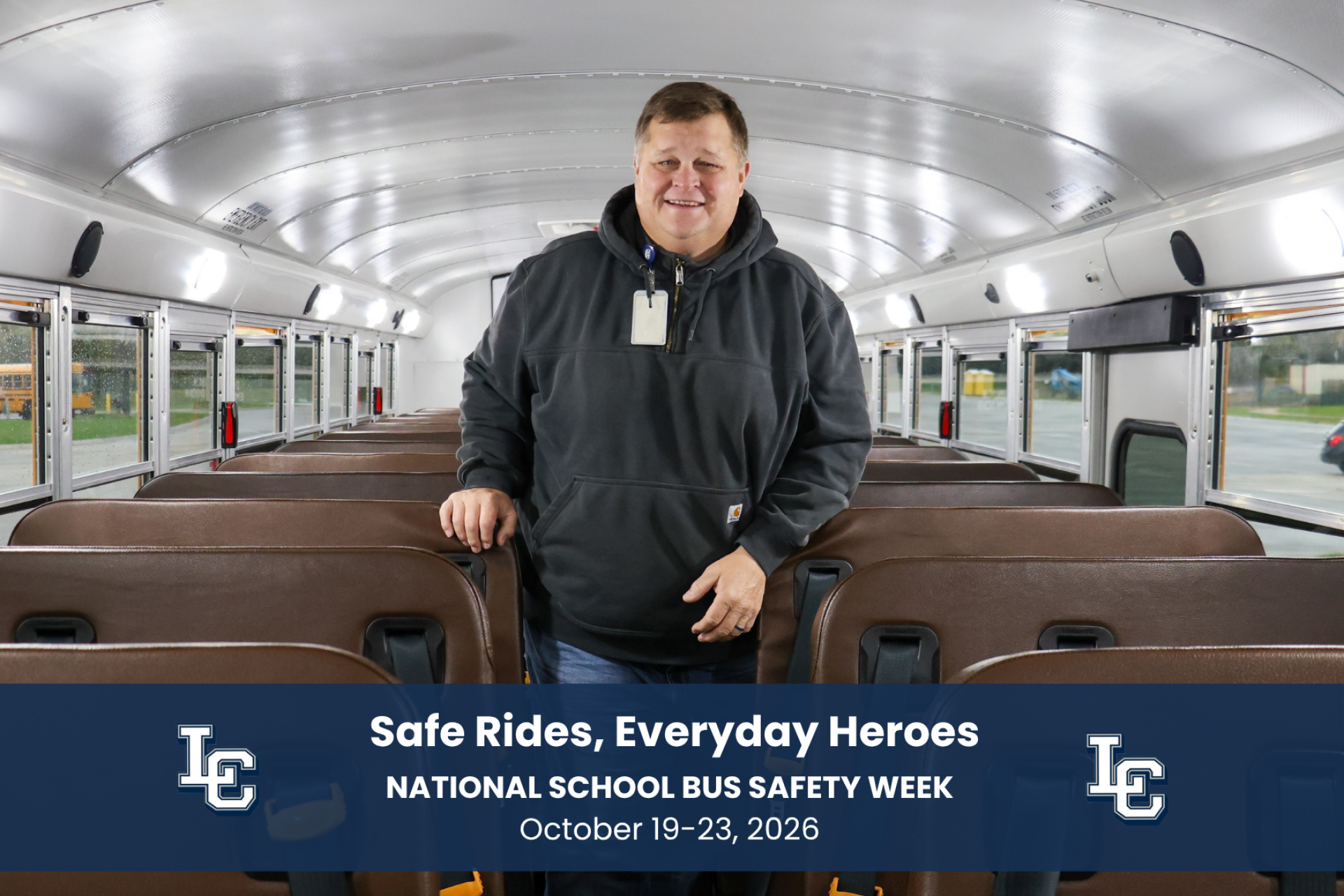 A school bus driver standing inside of the school bus, smiling at the camera.